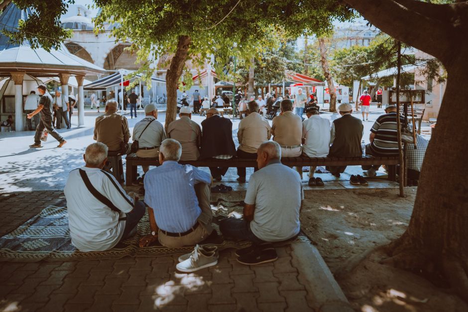 A group of senior men gather under the shade of a tree, enjoying a social moment outdoors.
