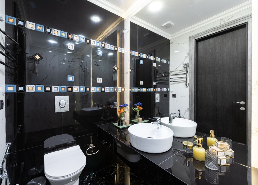 Interior of stylish restroom with white bidet installed at black tiled wall near flowers placed near sink at big mirror