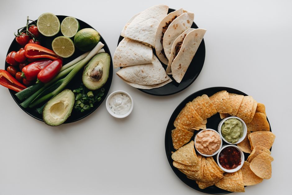 Mexican food setup with tacos, nachos, dips, and fresh vegetables for a vibrant meal.