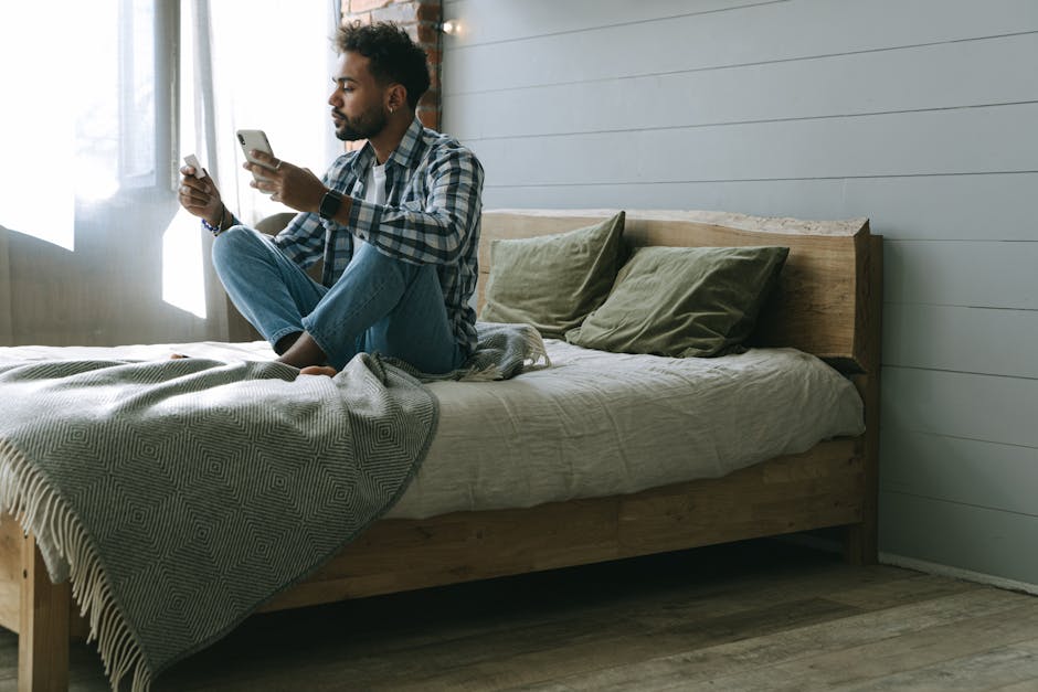 A man sits on a bed using a smartphone for online shopping and payments.