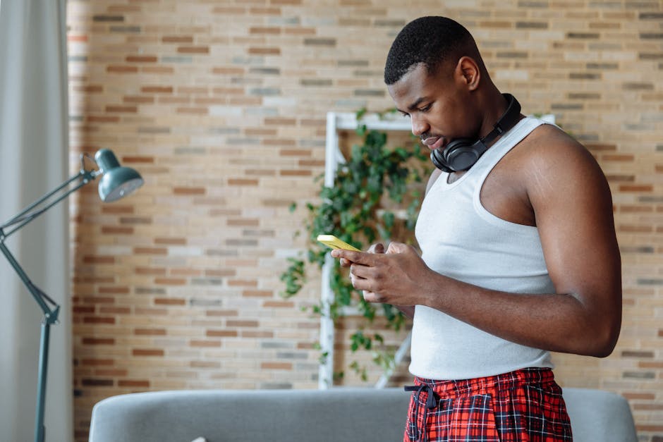 Casual young man using smartphone at home, wearing headphones.