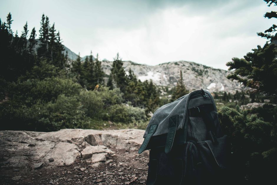 Backpack resting on rocky terrain amidst lush forest and mountain view.
