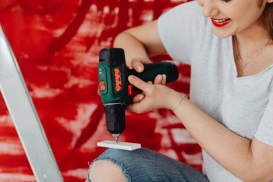 A smiling woman using a cordless drill, engaged in a home renovation project with a red background.