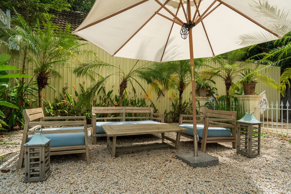 Cozy garden patio with wooden chairs, table, and umbrella surrounded by lush greenery.