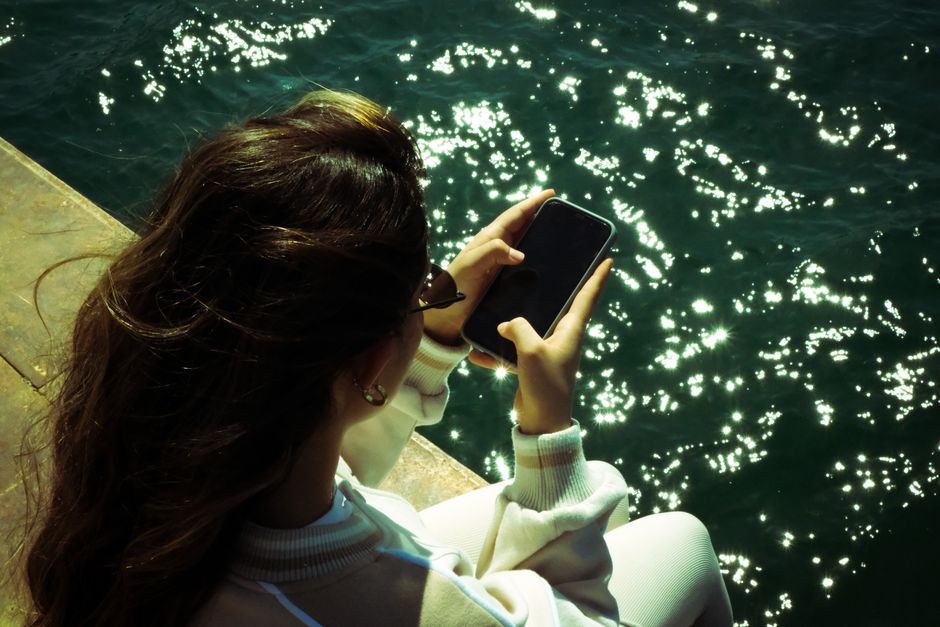 Woman taking photo with smartphone by sparkling water's edge.
