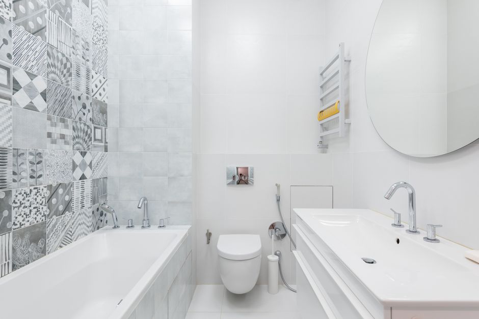Contemporary bathroom featuring white sanitaryware, a round mirror, and patterned wall tiles for a sleek design.