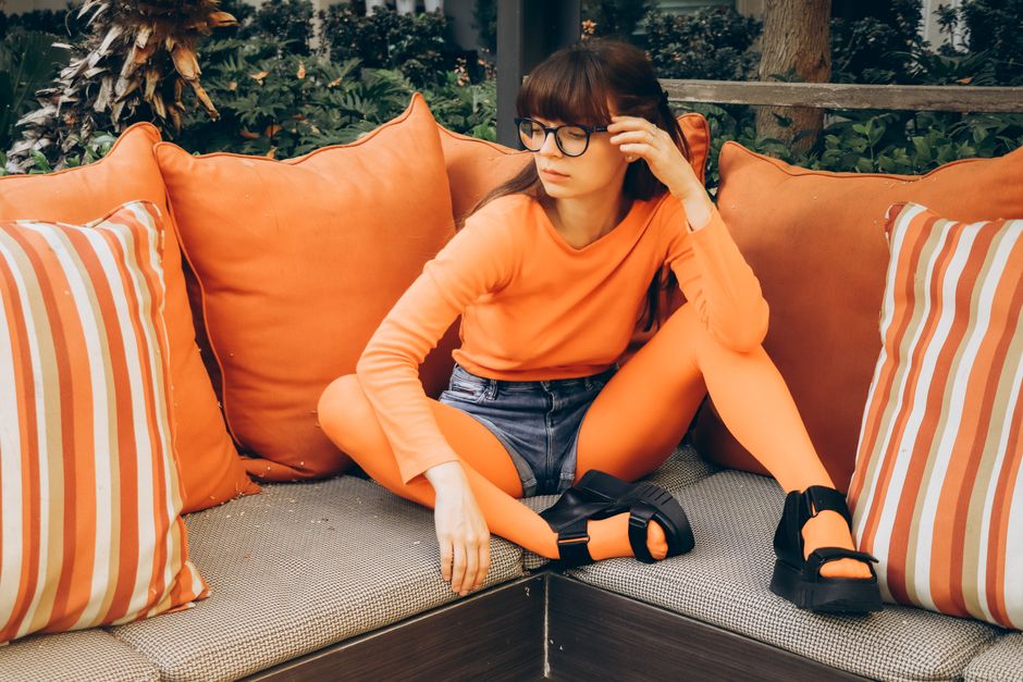 Fashionably styled woman in orange clothes sitting comfortably on an outdoor patio sofa.