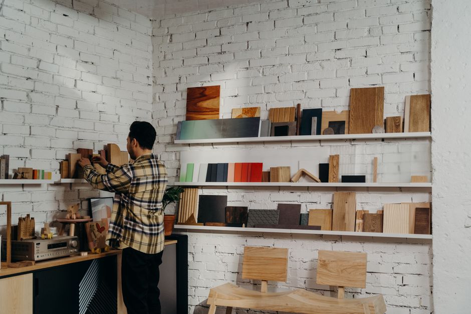 A man organizes wooden samples on shelves in a workshop, surrounded by tools and decor.