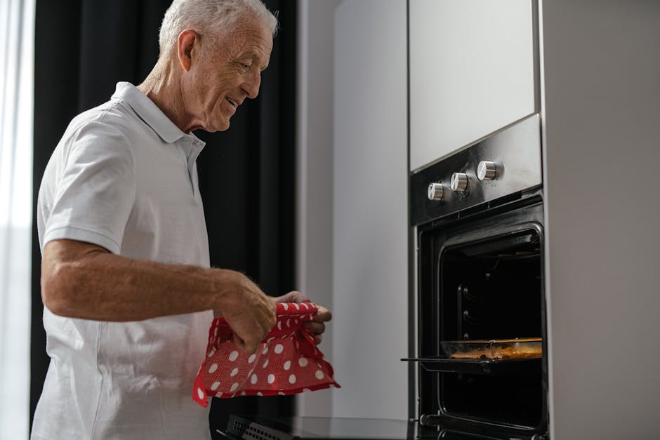 Senior man using an oven with a red polka dot cloth in a modern kitchen setting.