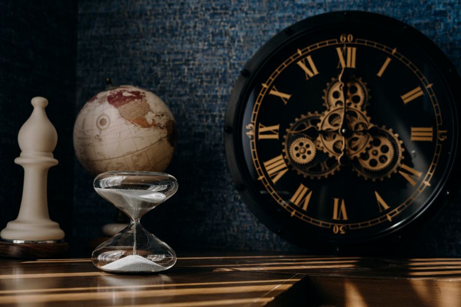 A dark and moody still life featuring an ornate clock, globe, and hourglass.