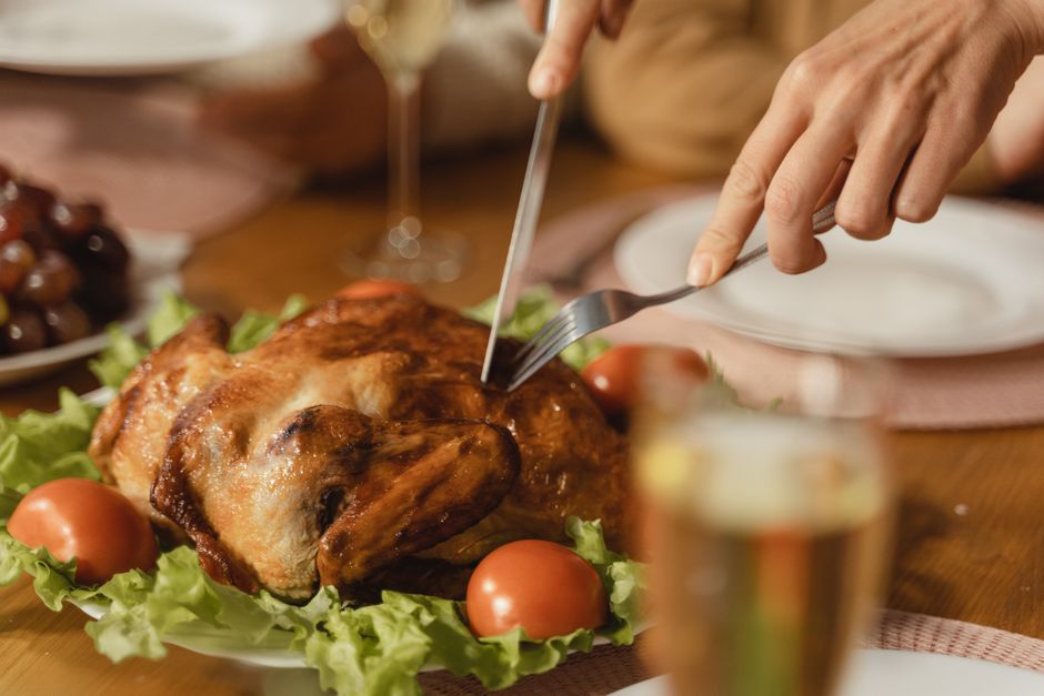 Close-up of hands slicing delicious roasted chicken with vegetables on a festive table setting.