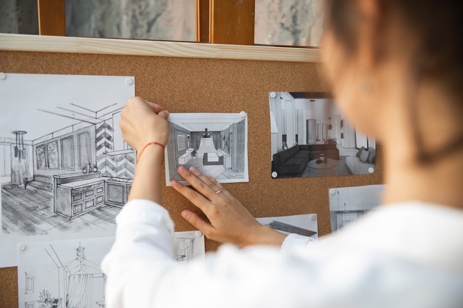 Person arranging interior design sketches on a corkboard indoors.