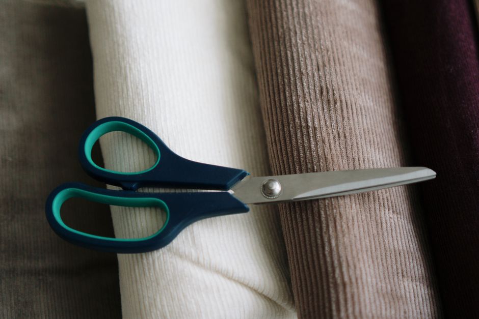 Top view of a pair of blue scissors resting on various colored velvet fabrics.