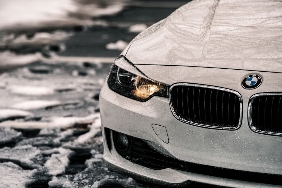 A front view of a car with headlights on, covered in frost, on a snowy road.