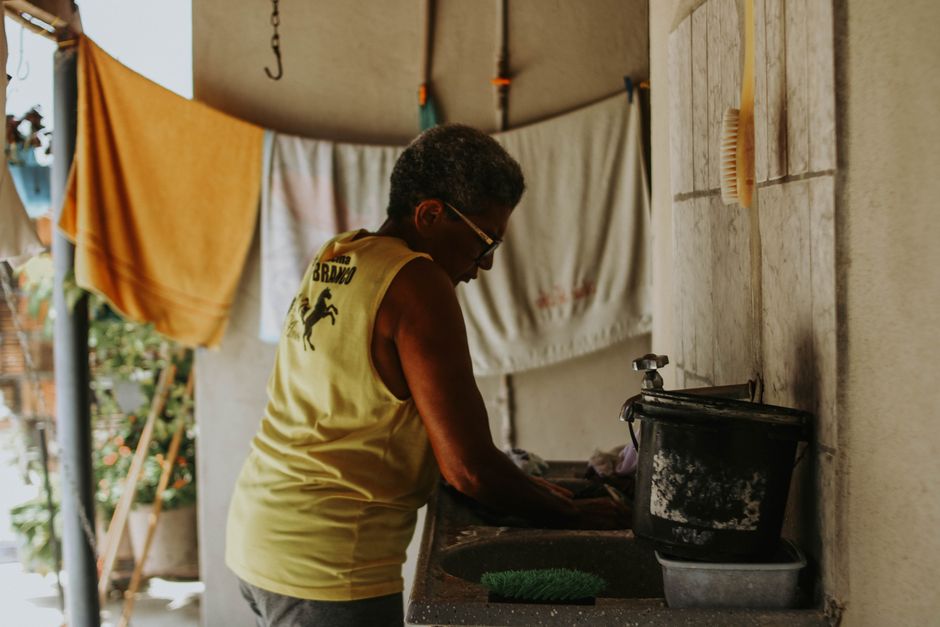 Elderly woman in yellow tank top washing dishes in a domestic setting.