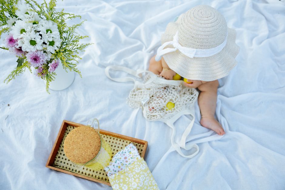 A baby sitting on a blanket outdoors with flowers and picnic items
