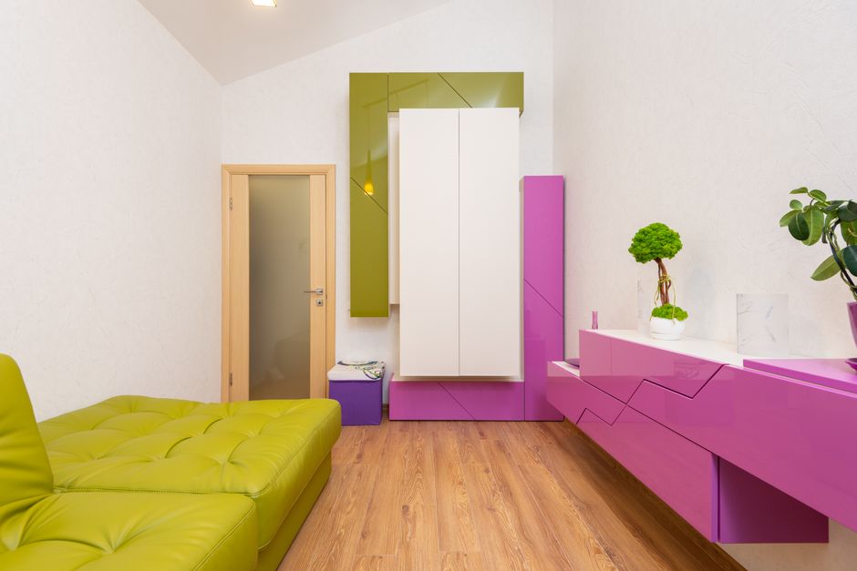 Interior of modern bedroom with comfortable green leather sofa and creative white and bright fuchsia colored furniture decorated with potted plants