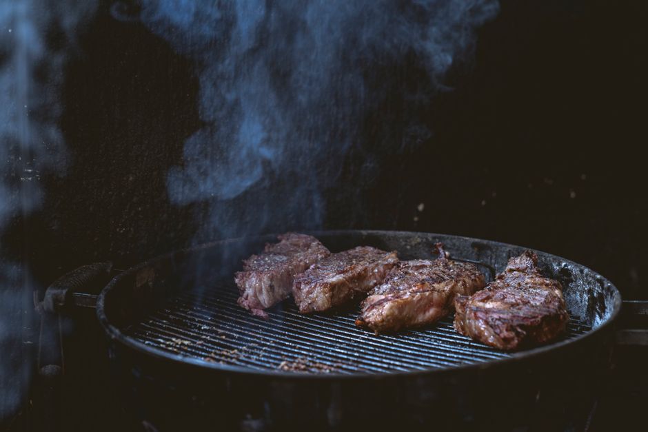 Close-up of juicy steaks grilling on a smoky barbecue, perfect for summer cookouts.