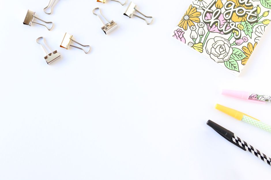 Top view of stationery items including clips and colorful pens on a white background with a decorative notepad.